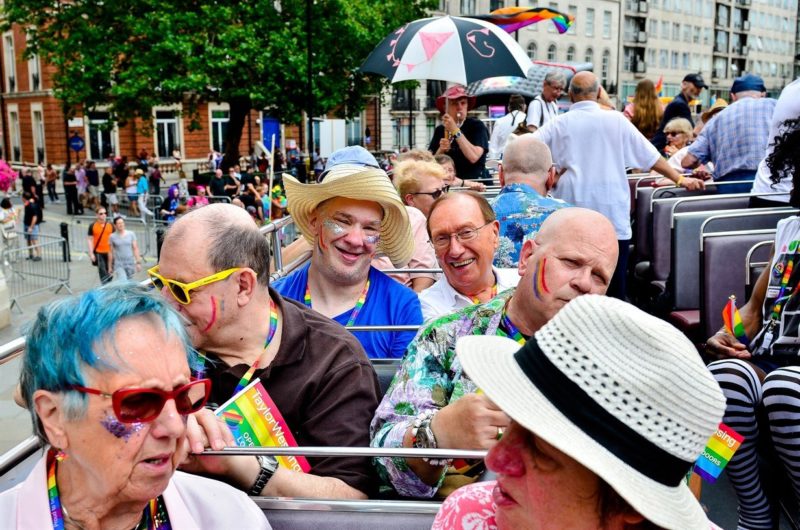 Photograph of Opening Doors charity enjoying Pride parade on an open top bus. Lots of colour and rainbows and happy people.